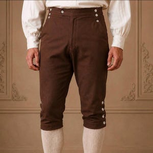 May include: Dark brown knee-length breeches featuring a high-waisted design with a button-front closure. The garment includes two rows of three small silver-toned buttons at the upper hip area and three silver-toned buttons at each outer knee.