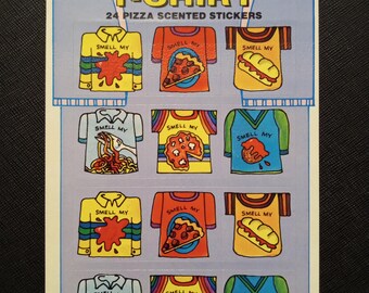 May include: A sheet of 24 pizza-scented scratch-and-sniff stickers. The stickers are shaped like t-shirts, each with a different pizza-themed design. The text "SMELL MY T-SHIRT" is printed on the sheet.