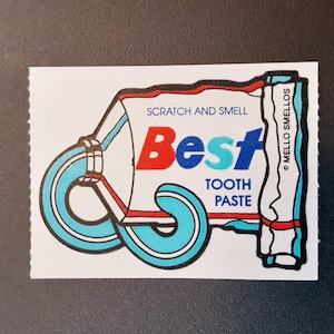 Puede incluir: Una pegatina de estilo vintage con un diseño de tubo de pasta de dientes. La palabra "Best" está en rojo y azul, con "Tooth Paste" debajo. La pegatina tiene una función "Scratch and Smell" y el texto "Mello Smellos".