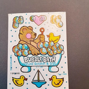 May include: A vintage sticker sheet featuring a brown bear in a blue bathtub with the words "Bubble Bath" and "Natural Scratch & Sniff." The sheet includes images of bubbles, ducks, a sailboat, and a heart. The sticker sheet is from 1983.