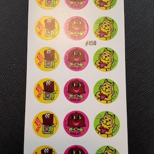 Puede incluir: Una hoja de pegatinas vintage con personajes de dibujos animados. Las pegatinas redondas presentan una barra de chocolate, un personaje sonriente y un gato sosteniendo un corazón. El texto incluye "1st RATE" y "GREAT". La hoja está etiquetada con "#850".