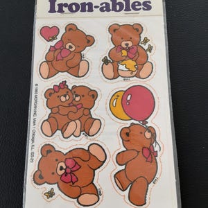 May include: A pack of vintage "Iron-ables" stickers. The stickers feature brown teddy bears with pink bows and hearts. The sheet includes the text "Scratch & Sniff" and "Iron-ables". There are six different bear designs, some with balloons and honey.