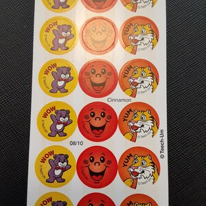 Puede incluir: Hoja de pegatinas vintage con personajes de dibujos animados. Los diseños incluyen un oso morado con pajarita, una cara sonriente y un tigre con un caramelo. Las pegatinas tienen las palabras "WOW" y "YUM".