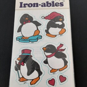 May include: A vintage sheet of "Iron-ables" with four cartoon penguins in different outfits, such as a bow tie, a Santa hat, a top hat, and a scarf. The sheet includes the text "Scratch & Sniff" and "Iron-ables".