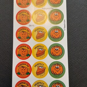 Puede incluir: Hoja de pegatinas con temática otoñal. Las pegatinas presentan una calabaza naranja sonriente, una porción de pastel de calabaza y las palabras "Pumpkin Pie" y "Perfect". Las pegatinas son redondas y tienen una combinación de colores rojo, amarillo y verde.