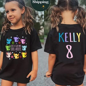 May include: Black t-shirt with a colourful axolotl design and the words "JUST A GIRL WHO LOVES AXOLOTLS". The back of the shirt has the name "KELLY" and the number "8" in different colours.