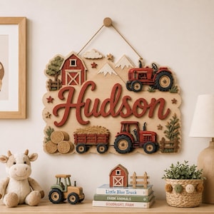 Puede incluir: Un adorno de pared de madera con el nombre Hudson en letras rojas grandes. El diseño incluye un granero rojo, dos tractores rojos, pacas de heno, montañas y estrellas. Está colgado con una cuerda marrón y tiene un fondo de madera clara.