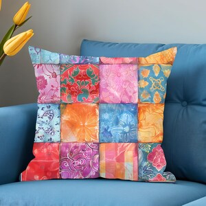 Peut inclure: Coussin carré avec un motif patchwork. Le coussin présente une variété de carrés floraux et à motifs colorés dans les tons de rose, d'orange, de bleu et de rouge. Le coussin est placé sur un canapé bleu.