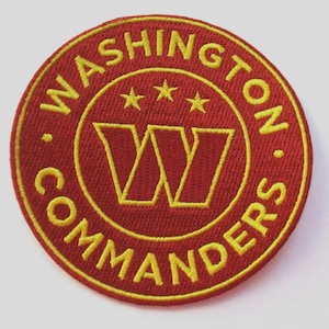 Può includere: Una toppa rotonda ricamata con le parole "WASHINGTON COMMANDERS" in giallo, che circondano un logo a doppia "W" giallo e tre stelle, il tutto su sfondo rosso.