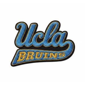 Puede incluir: Parche bordado con el texto "UCLA BRUINS" en hilo azul y dorado sobre fondo negro. "UCLA" está en una fuente cursiva, y "BRUINS" en letras de bloque.