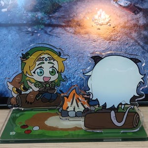 May include: Acrylic stand featuring two anime-style characters sitting by a campfire. One character has green hair and a leaf crown, the other has white hair and cat ears. The base is green with cartoon tomatoes and flowers.
