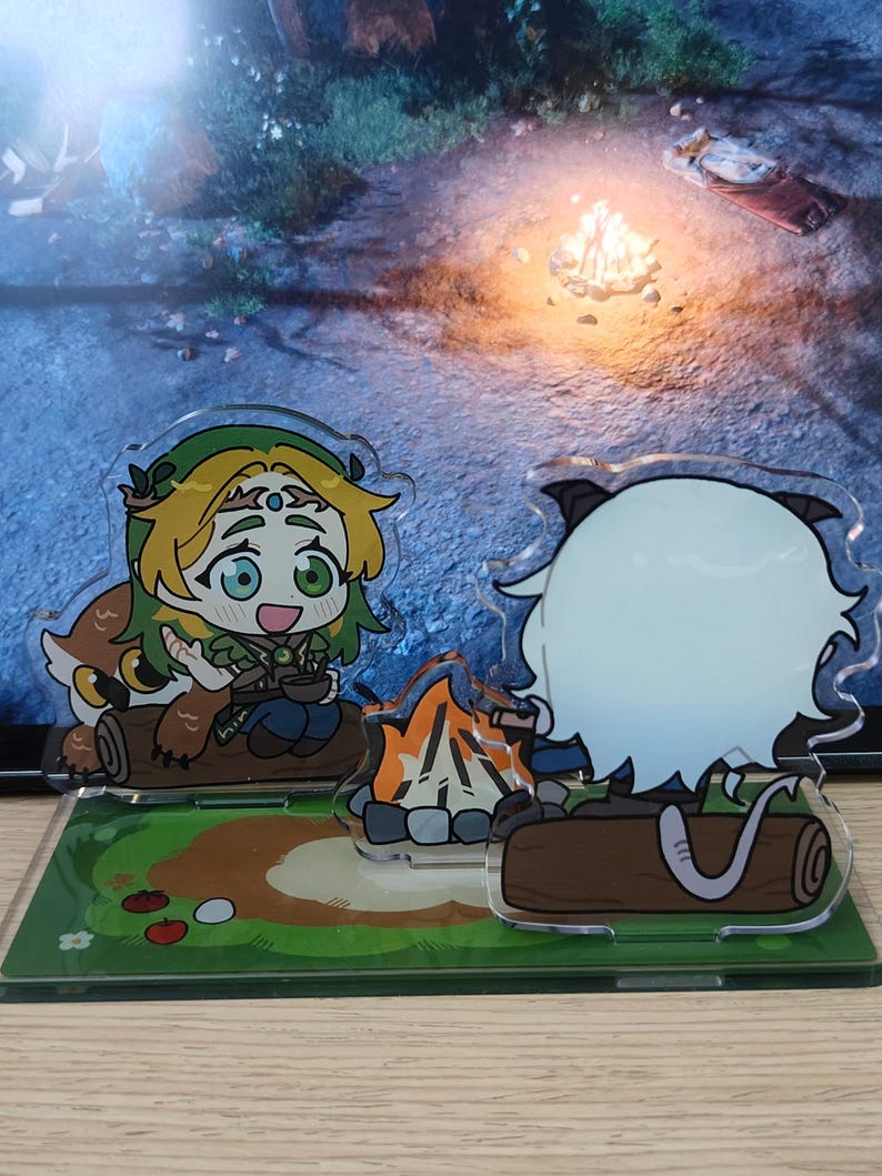 May include: Acrylic stand featuring two anime-style characters sitting by a campfire. One character has green hair and a leaf crown, the other has white hair and cat ears. The base is green with cartoon tomatoes and flowers.