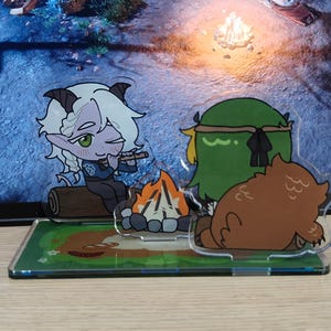 May include: Acrylic figurines depicting a campfire scene with cartoon characters. One figure is a light-skinned character with white hair and horns playing a flute. Another is a green character with a headband, and a brown bear figure.