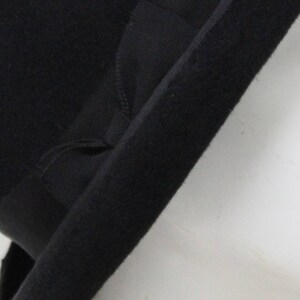 May include: A black felt hat featuring a wide, structured brim and a matching black grosgrain ribbon band wrapped around the base of the crown. The material has a soft, matte texture, and the ribbon includes a small, folded bow detail.