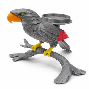 May include: A gray parrot-shaped decorative tray with an orange beak, yellow feet, and red accents on the tail. The bird is perched on a gray branch, and the tray is located on the bird's back.