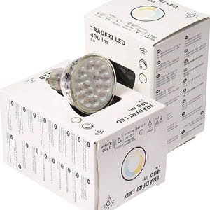 Può includere: Una lampadina LED trasparente con più luci piccole è mostrata accanto a due scatole bianche. Le scatole hanno il testo "TRÅDFRI LED 400 lm 5W" stampato. La lampadina è con attacco GU10.