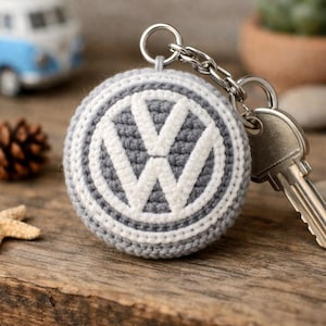 Könnte beinhalten: Eine weiße Keramik-Tasse mit schwarzem Henkel und dem Text "But First, Coffee" in fetter, schwarzer Schrift. Die Tasse steht vor einem verschwommenen Hintergrund, der eine gemütliche Umgebung suggeriert.