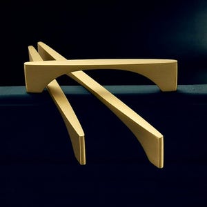 May include: Gold-coloured cabinet pulls with an arched design. The hardware is displayed against a dark blue background, showcasing the sleek, modern aesthetic of the furniture accessories. The pulls have a smooth, matte finish.