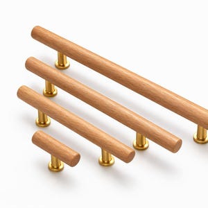 May include: Five wooden cabinet handles with brass-coloured bases. The cylindrical handles vary in length, with the longest measuring approximately 30 cm. The wood has a natural, light brown colour.