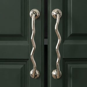 May include: Close-up of two dark green cabinet doors with silver wavy handles. The handles have a decorative, curved design and are mounted on round, silver bases. The doors have a recessed panel design.