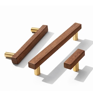 May include: Three wooden cabinet pulls with brass-colored cylindrical posts. The pulls are rectangular and made of dark brown wood. The cabinet hardware is displayed on a white background.