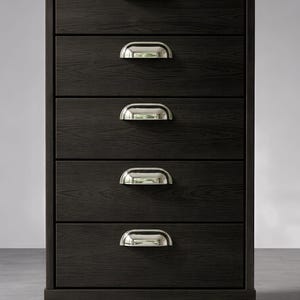 Puede incluir: Una cómoda de cinco cajones de color marrón oscuro con tiradores plateados en forma de media luna. La cómoda tiene una textura de vetas de madera y se apoya sobre patas cortas y negras. Los cajones están espaciados uniformemente, el diseño es moderno y minimalista.