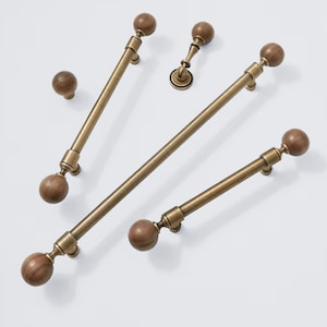 May include: A selection of cabinet hardware in a warm brass finish. The set includes bar pulls with wooden ball ends, a knob, and a smaller pull. The hardware is designed for a classic, elegant aesthetic.