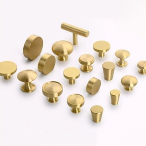 May include: A collection of various brass cabinet knobs and pulls. The hardware includes round, cylindrical, and bar-shaped designs in a warm gold tone. These decorative knobs and pulls are suitable for furniture and cabinetry.