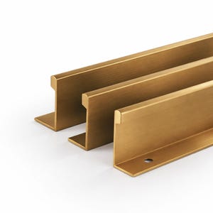 May include: Three brass-coloured cabinet pulls arranged diagonally against a white background. Each pull has a rectangular bar with a right-angle base, and a single pre-drilled hole. The pulls have a brushed finish and a modern design.