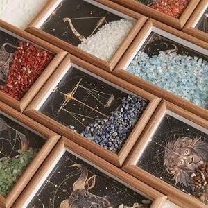 May include: Wooden framed art pieces featuring zodiac constellations and colorful gemstones. Each frame displays a different astrological sign with a unique arrangement of stones in various colors, including red, blue, and white. The artwork is set against a dark background.