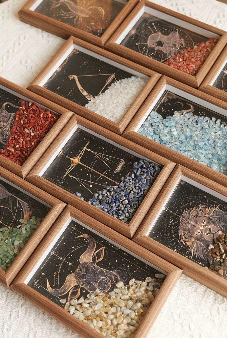 May include: Wooden framed art pieces featuring zodiac constellations and colorful gemstones. Each frame displays a different astrological sign with a unique arrangement of stones in various colors, including red, blue, and white. The artwork is set against a dark background.