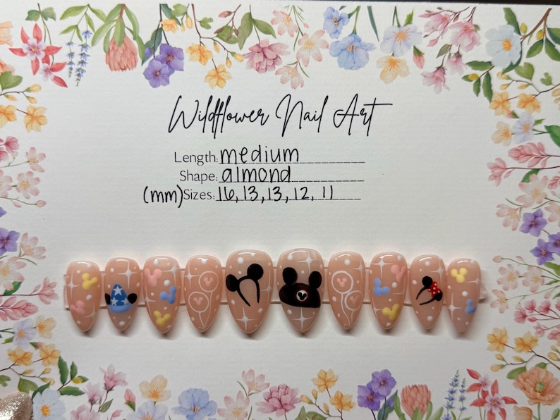 May include: Almond-shaped, medium-length press-on nails with a light pink base. Each nail features a unique design, including Mickey Mouse, hearts, and stars. The set is labeled "Wildflower Nail Art" with size details in millimeters.