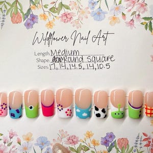 May include: A set of medium-length, round square press-on nails with various designs. The nails feature a nude base with colorful tips, including floral, polka dot, and character-themed art. The text "Wildflower Nail Art" is visible.