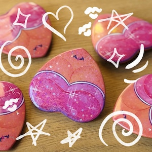 May include: Heart-shaped stickers with a two-tone design in shades of pink and orange, adorned with glitter and star accents. The stickers feature a bat graphic and are surrounded by white doodle art.
