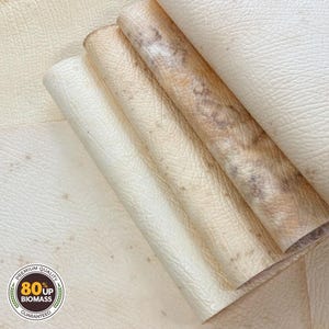 May include: Close-up of several rolled sheets of off-white and tan leather. The leather has a textured surface and varying shades of color. The image includes a circular logo with the text "Premium Quality 80% Up Biomass Guaranteed."