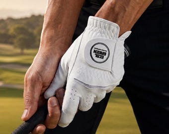 May include: White golf glove with the text "ECOL GREEN" in a black circle. The glove is being held on a golf club. The glove has small perforations for breathability. The background is a golf course.