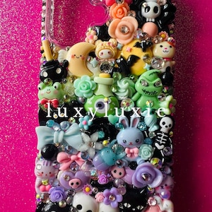 Puede incluir: Una funda de teléfono decorada con una densa disposición de dijes de plástico coloridos que incluyen una estrella rosa, una luna creciente, un conejo azul, calaveras, flores y varios personajes, intercalados con pedrería y el texto luxyluxie.