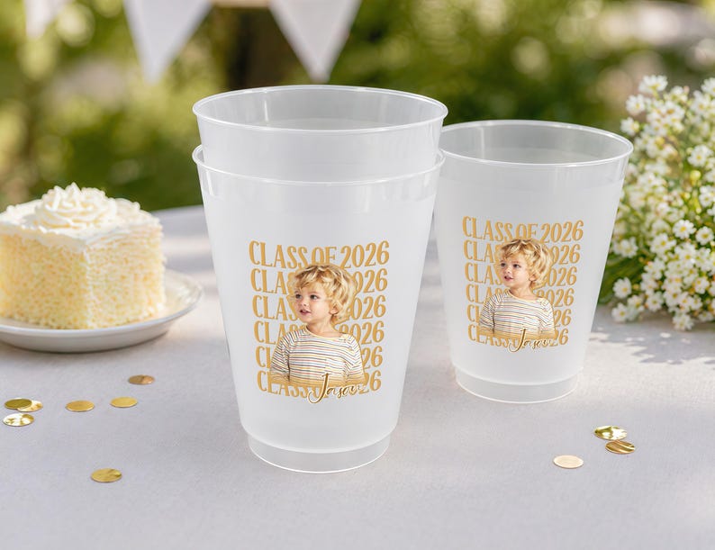 May include: Three frosted plastic cups with a gold design. The design includes the text "CLASS OF 2026" and a photo of a child. The cups are on a white surface with gold confetti and a piece of cake.