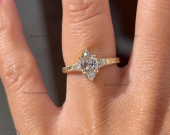 May include: A gold ring featuring a central marquise-cut gemstone held by a prong setting. The band is decorated with small, round accent stones embedded along the shoulders, creating a textured, metallic finish across the entire ring structure.
