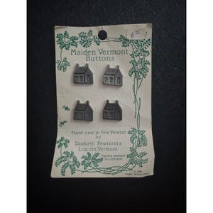 May include: Four house-shaped pewter buttons attached to a cream-colored card with green vine illustrations. The card text reads Maiden Vermont Buttons, Hand-cast in fine Pewter by Danforth Pewterers, Lincoln, Vermont, Machine washable, Dry cleanable.