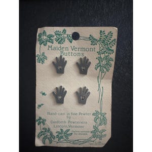 May include: Four silver-toned hand-shaped pewter buttons attached to a beige card with green botanical illustrations. The card reads Maiden Vermont Buttons, Hand-cast in fine Pewter by Danforth Pewterers, Lincoln, Vermont, Machine washable, Dry cleanable.