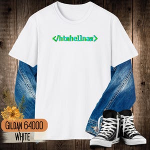 Op de afbeelding: Een wit T-shirt met korte mouwen en de groene tekst htmhellnaw tussen punthaken op de borst. Het shirt is gelaagd over een blauw spijkerjack en gecombineerd met zwart-witte hoge sneakers. De tekst luidt GILDAN 64000 WHITE.