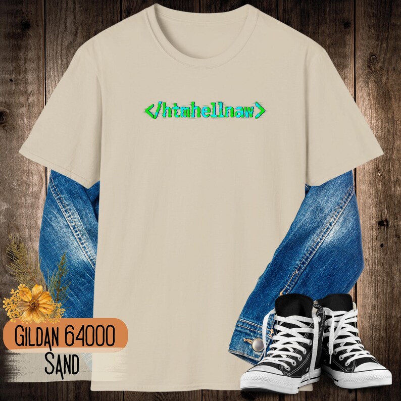 Op de afbeelding: Een zandkleurig t-shirt met korte mouwen en de tekst htmhellnaw tussen groene en blauwe code-haakjes op de borst. Het shirt is gelaagd over een blauw spijkerjack en gecombineerd met zwart-witte hoge canvas sneakers.