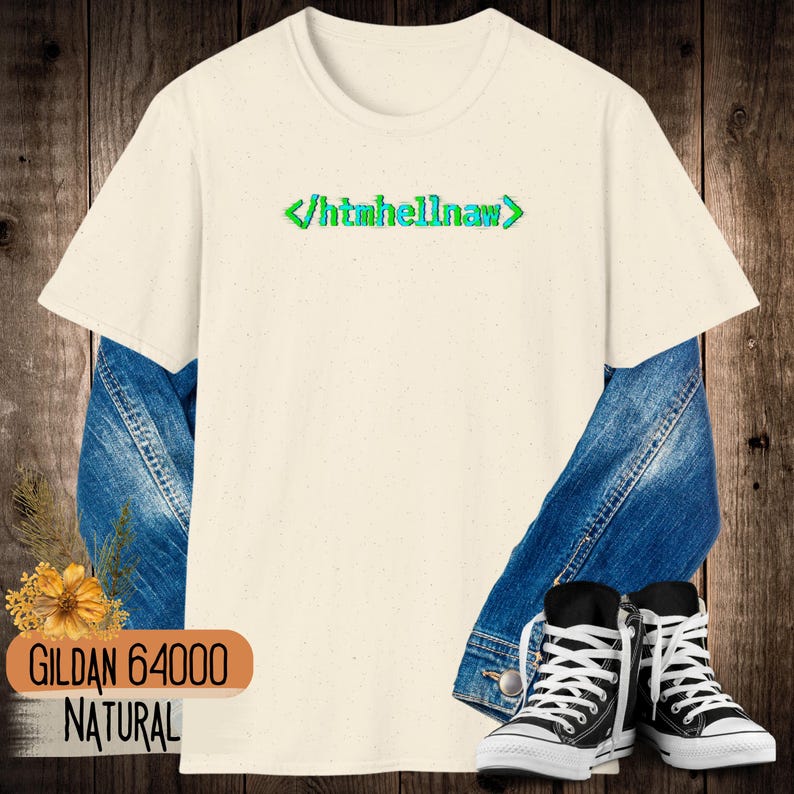 Op de afbeelding: Een naturelkleurig T-shirt met korte mouwen en de tekst "</htmhellnaw>" in een groen en blauw gepixeld lettertype in het midden op de borst. Het T-shirt is gelaagd over een blauw spijkerjack en gecombineerd met zwart-witte hoge sneakers.