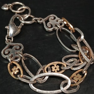 Puede incluir: Pulsera plateada con detalles dorados. La pulsera presenta una mezcla de eslabones ovalados y decorativos, con cierre de mosquet&oacute;n. Algunos eslabones tienen un dise&ntilde;o floral.