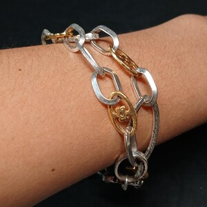 Puede incluir: Pulsera de cadena plateada y dorada. La pulsera presenta una mezcla de eslabones ovalados plateados y eslabones decorativos dorados. Los eslabones dorados tienen un dise&ntilde;o floral. La pulsera se lleva en la mu&ntilde;eca.