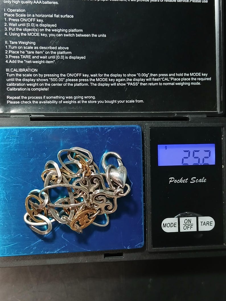 Puede incluir: Un collar plateado y dorado con un cierre en forma de coraz&oacute;n se muestra en una b&aacute;scula digital de bolsillo. La b&aacute;scula muestra un peso de 25,2 gramos. La b&aacute;scula tiene un bot&oacute;n de encendido/apagado y un bot&oacute;n de tara.