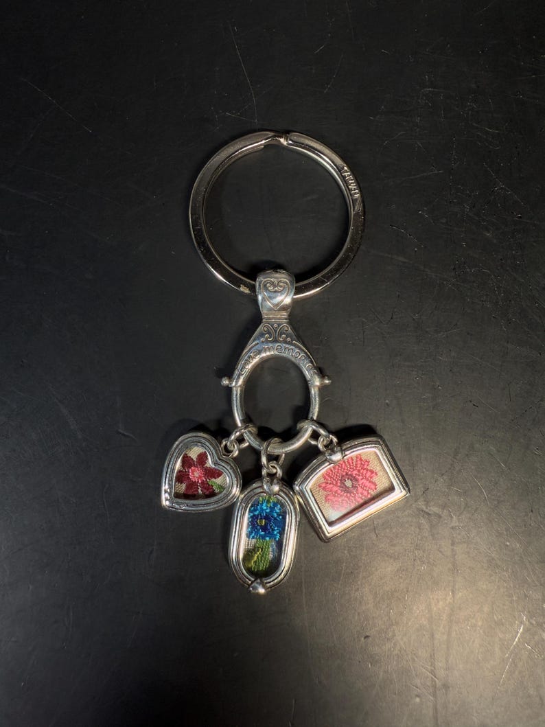 May include: Silver-toned keychain with three charms. The charms are a heart, an oval, and a rectangle, each containing a colorful floral design. The keychain has a large ring and a decorative clasp.