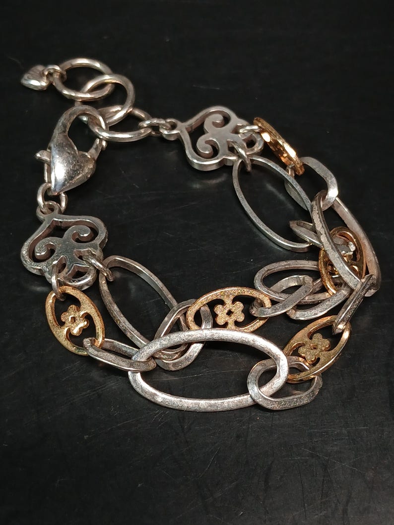 Puede incluir: Pulsera plateada con detalles dorados. La pulsera presenta una mezcla de eslabones ovalados y decorativos, con cierre de mosquet&oacute;n. Algunos eslabones tienen un dise&ntilde;o floral.