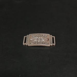 May include: A silver-toned metal bar with the words "FLOWER HONOR CLUB" engraved on it. The bar has a rectangular shape with a flower design in the center and two rectangular loops on each end.